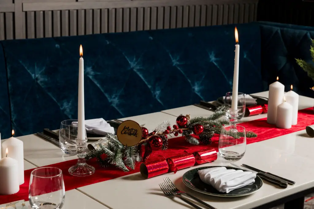 Christmas dining table with candles, red decorations and festive greenery beside blue banquette seating