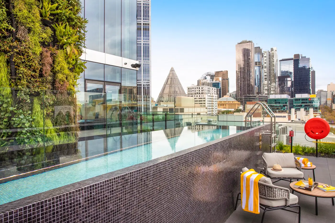 Rooftop infinity pool at voco Melbourne Central, framed by a living green wall with views across the Melbourne CBD skyline