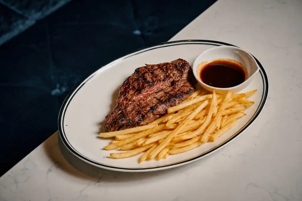 Grilled steak served with fries and a bowl of sauce on a white plate