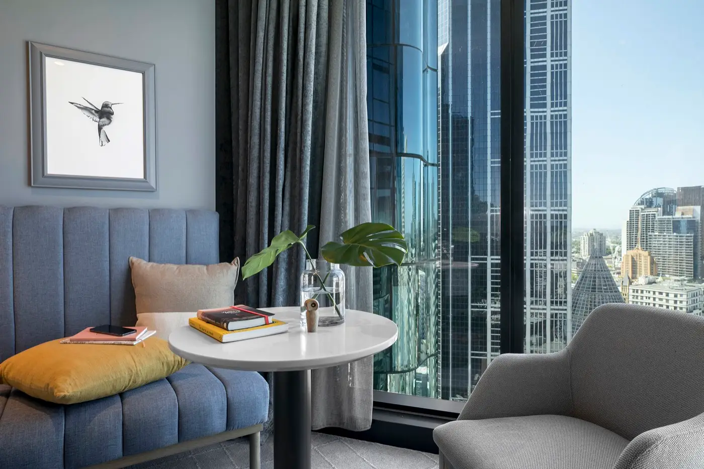 Sofa, armchair and round table beside floor-to-ceiling windows overlooking Melbourne city buildings