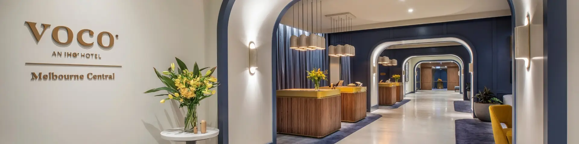 Reception area at voco Melbourne Central with curved archways, timber desks and floral arrangements