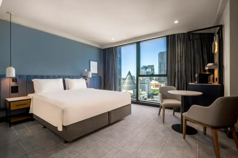 Guest room with a large bed, table and chairs, coffee station and view towards the Melbourne Central Shot Tower cone