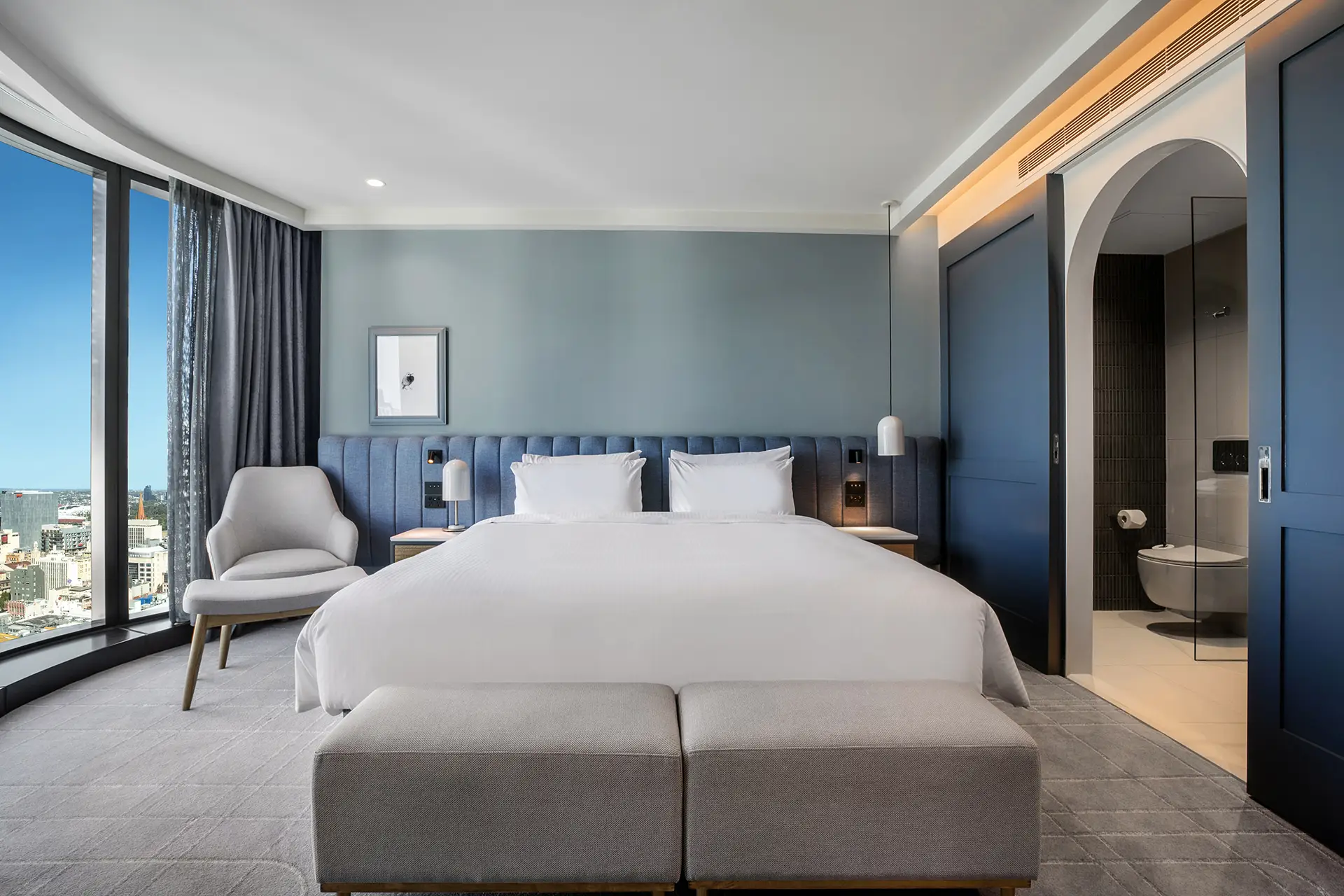 King guest room with bench seating, armchair, city views and an open bathroom entrance