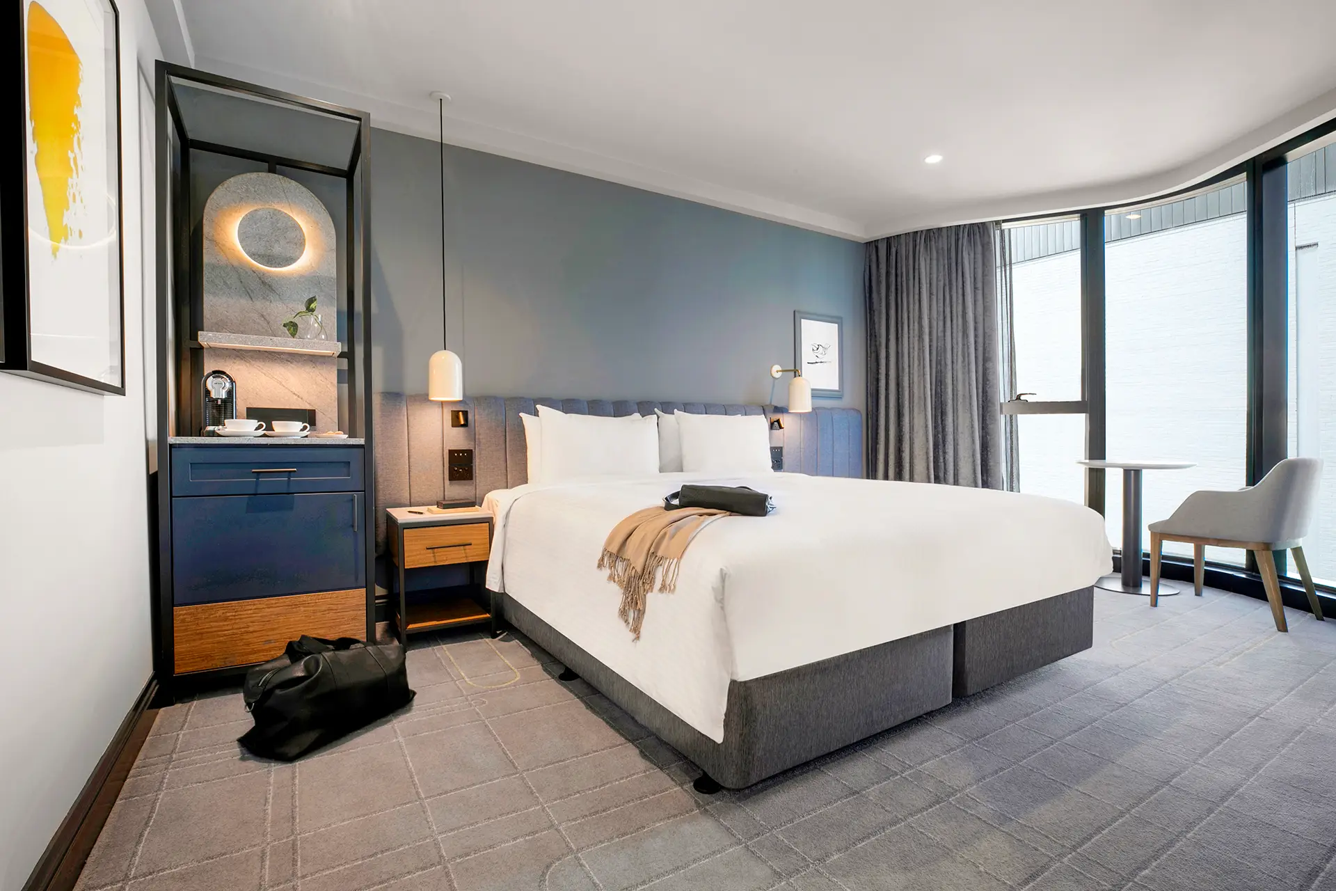 Guest room with a large bed, blue upholstered headboard, coffee station and curved floor-to-ceiling windows