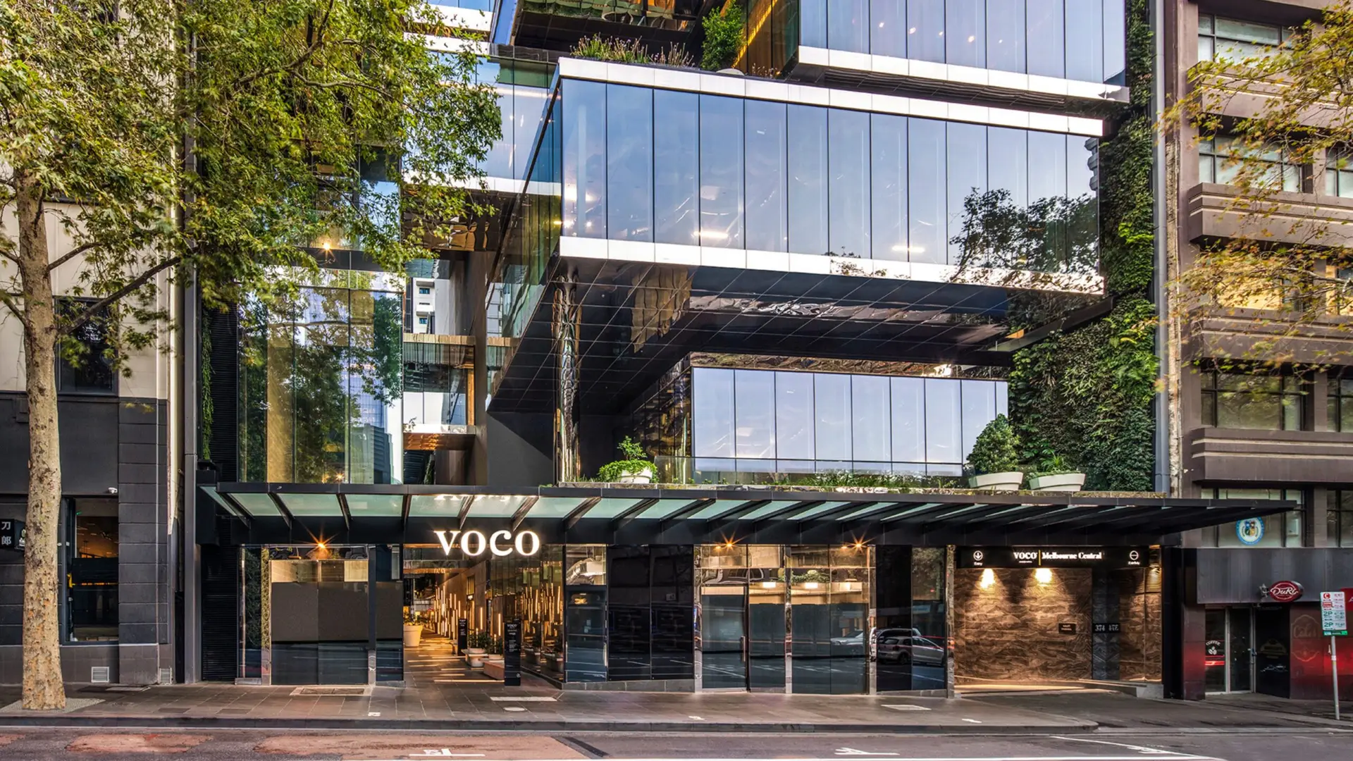 Exterior of voco Melbourne Central with glass façade, greenery and street-level entrance
