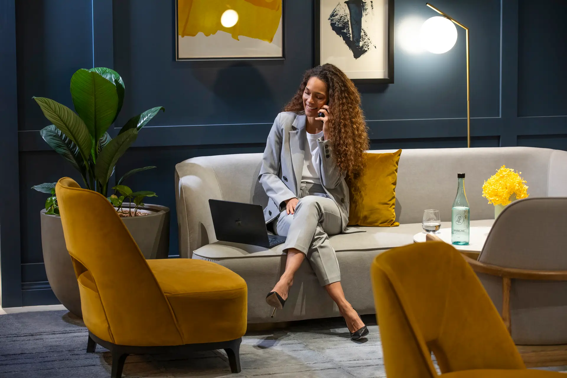 Guest seated with a laptop in a stylish lounge with mustard chairs and dark blue walls
