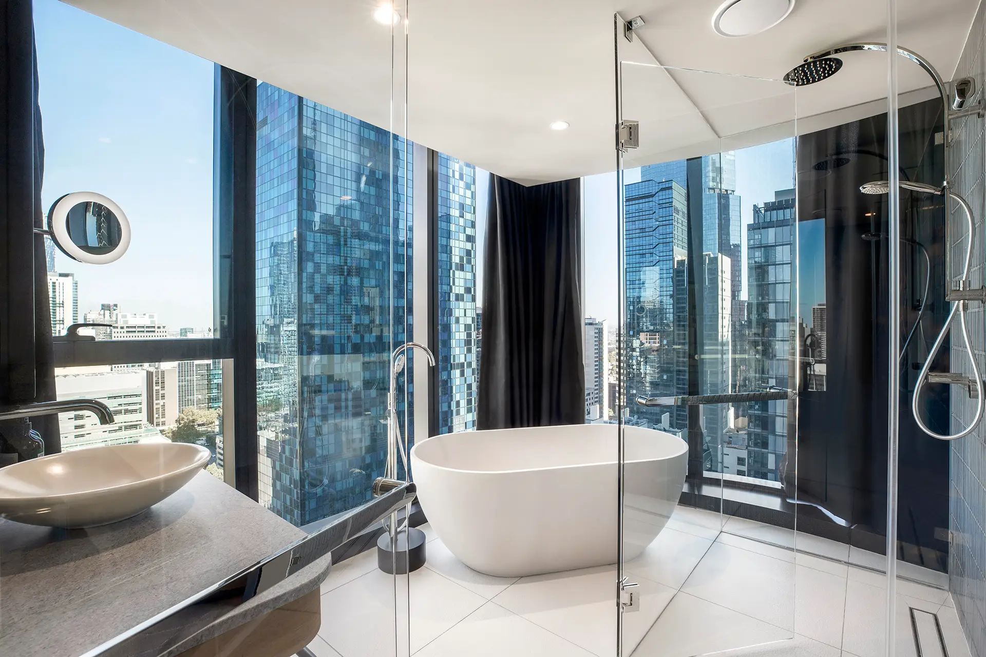 Bathroom with freestanding bath, glass shower and floor-to-ceiling windows overlooking the city