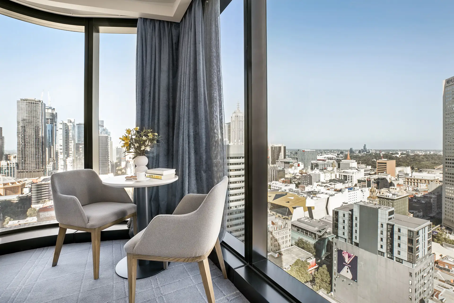 Two chairs and a round table beside curved windows with an elevated view across Melbourne