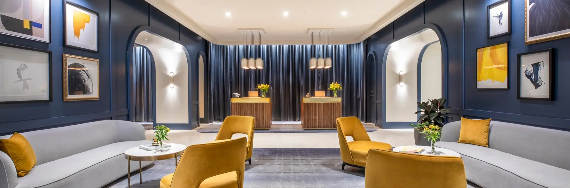 Hotel lobby with blue walls, mustard armchairs, grey sofas, artwork and reception desks