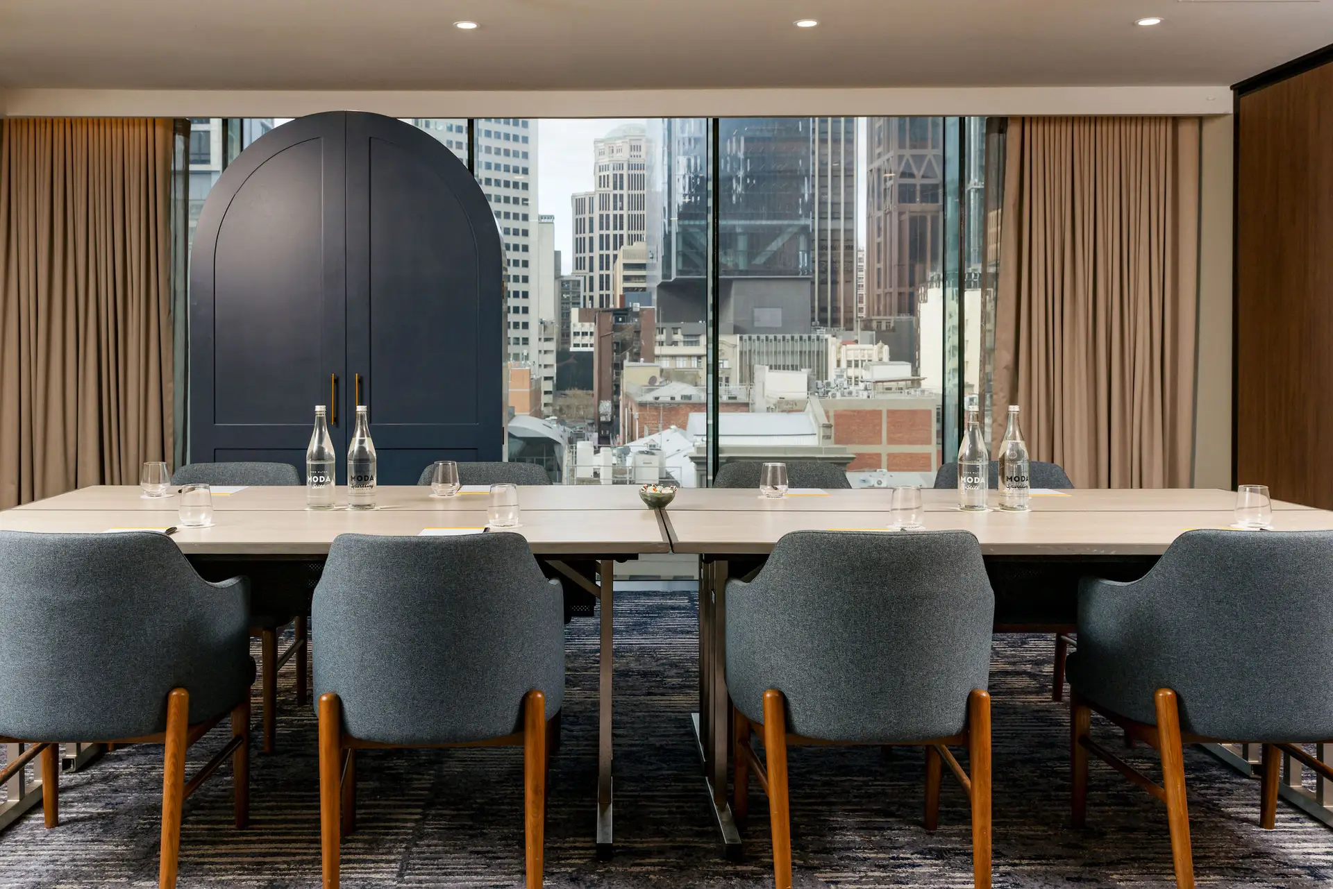 Meeting room with a long conference table, grey chairs and floor-to-ceiling windows overlooking the city
