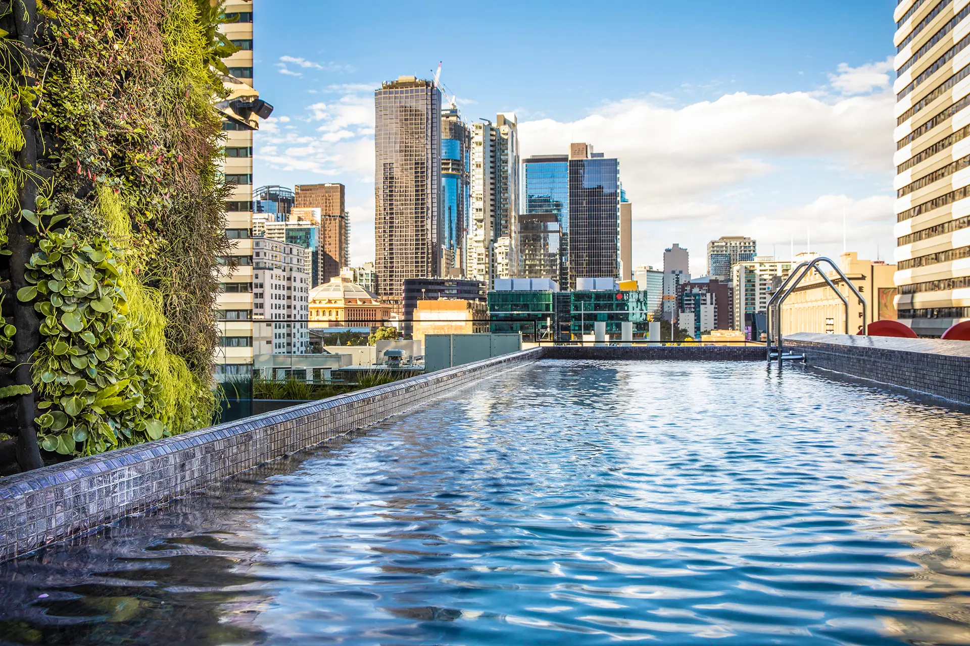 Rooftop swimming pool beside a vertical garden with views across central Melbourne