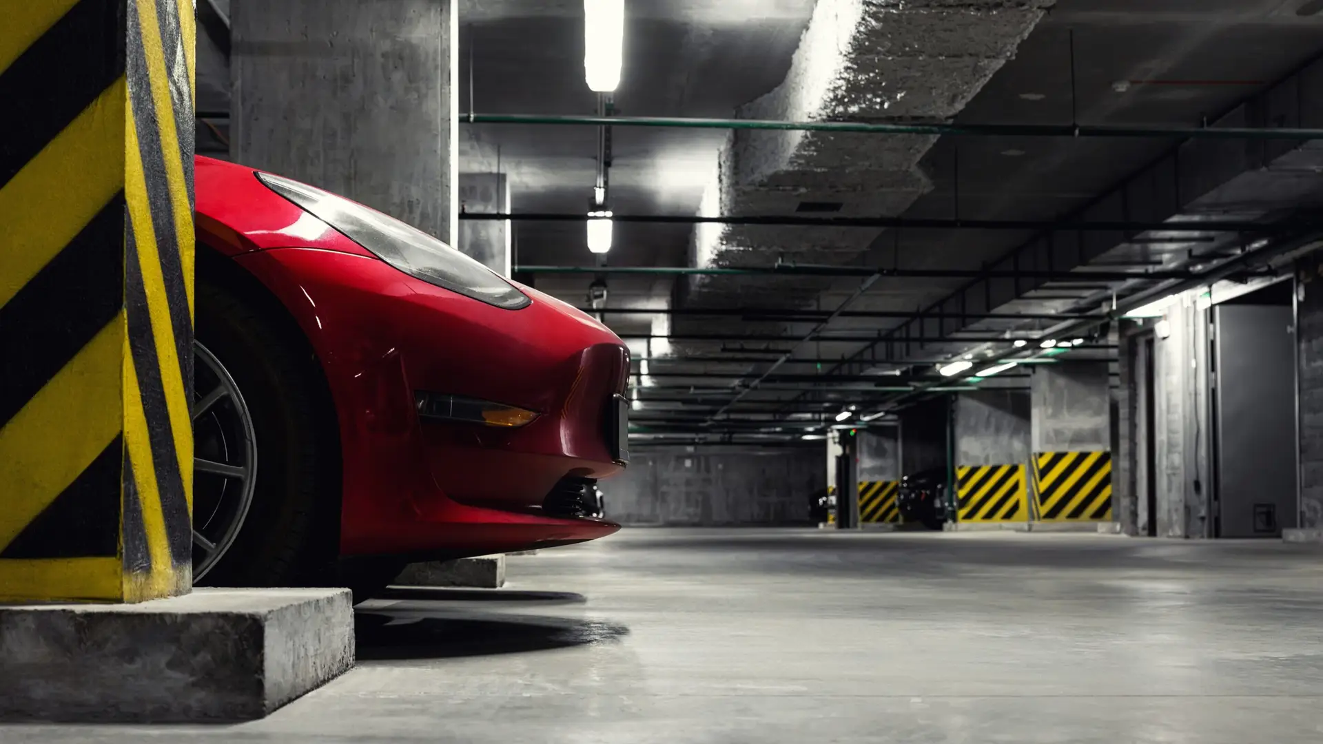 Red car parked in an underground car park with concrete pillars and overhead lighting