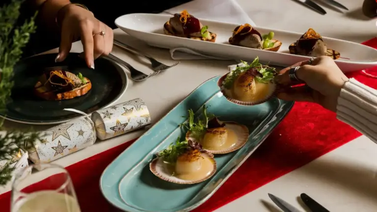 Festive shared dining table with scallops, canapés and guests serving plated dishes