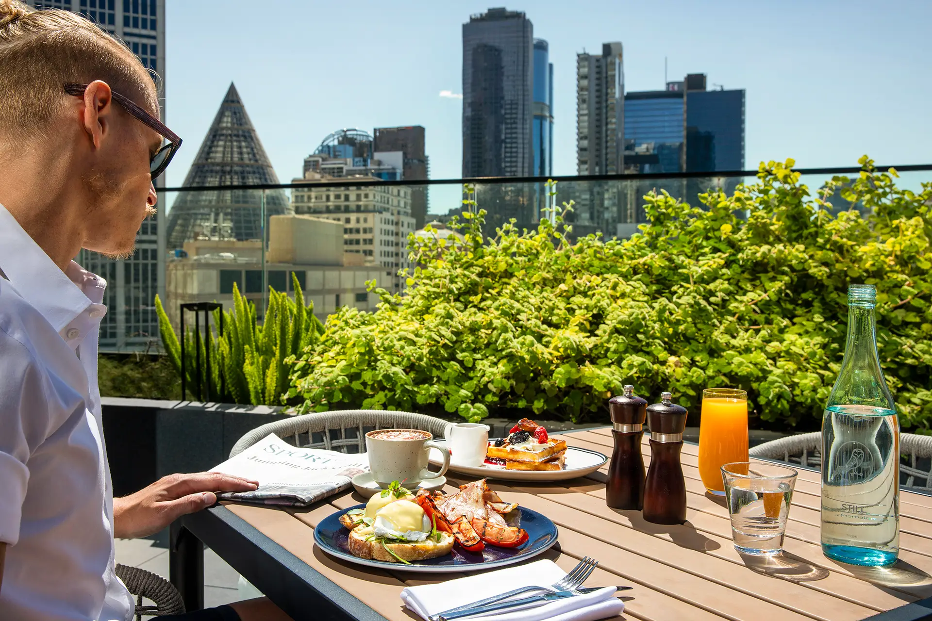Guest enjoying breakfast with coffee and juice on a sunny terrace overlooking Melbourne buildings