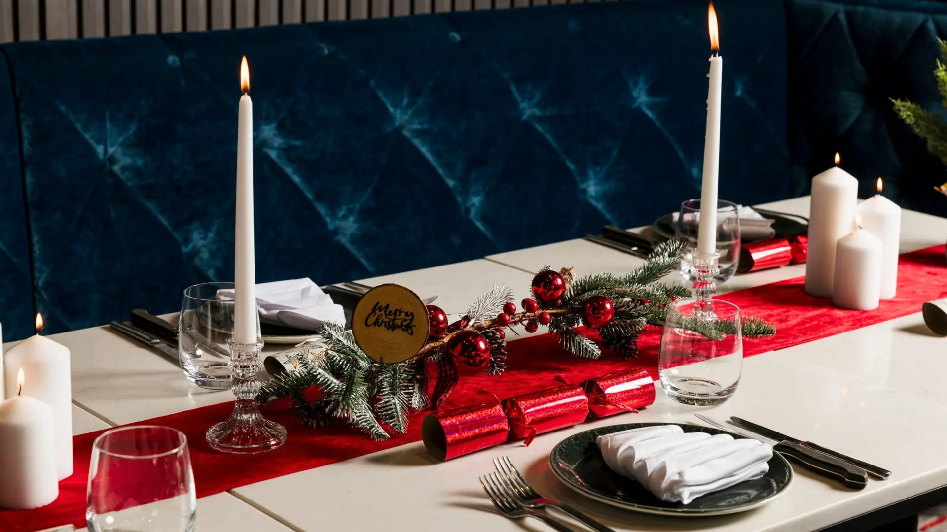 A Christmas table set with candles, crackers and a red runner