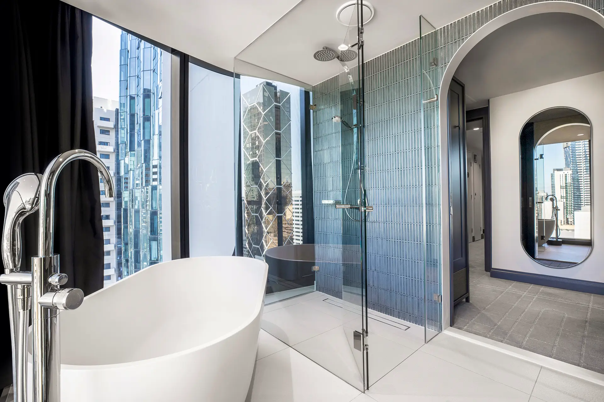 Modern hotel bathroom with freestanding bath, glass shower and city views