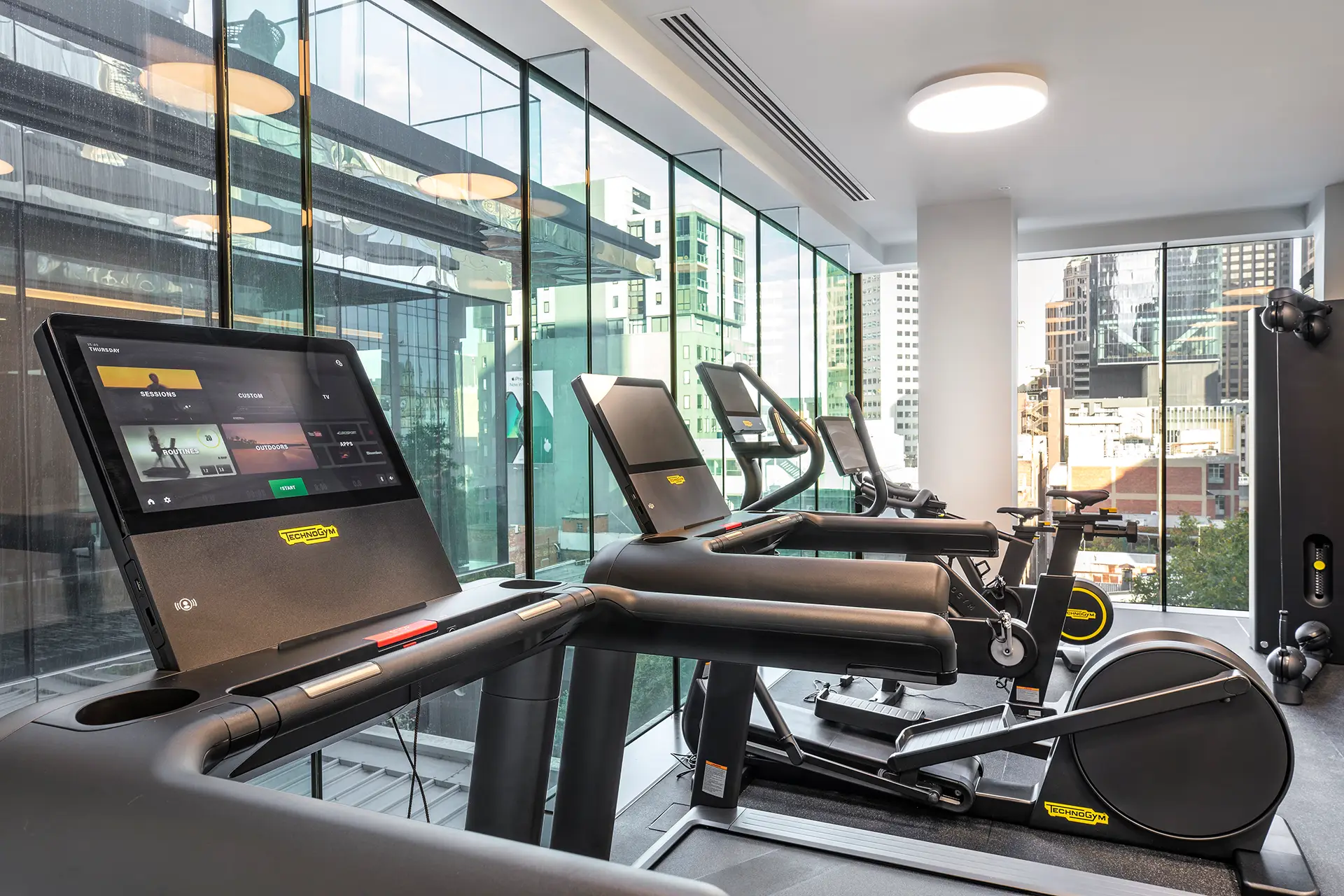 Fitness centre with treadmills, exercise bikes and floor-to-ceiling windows overlooking Melbourne