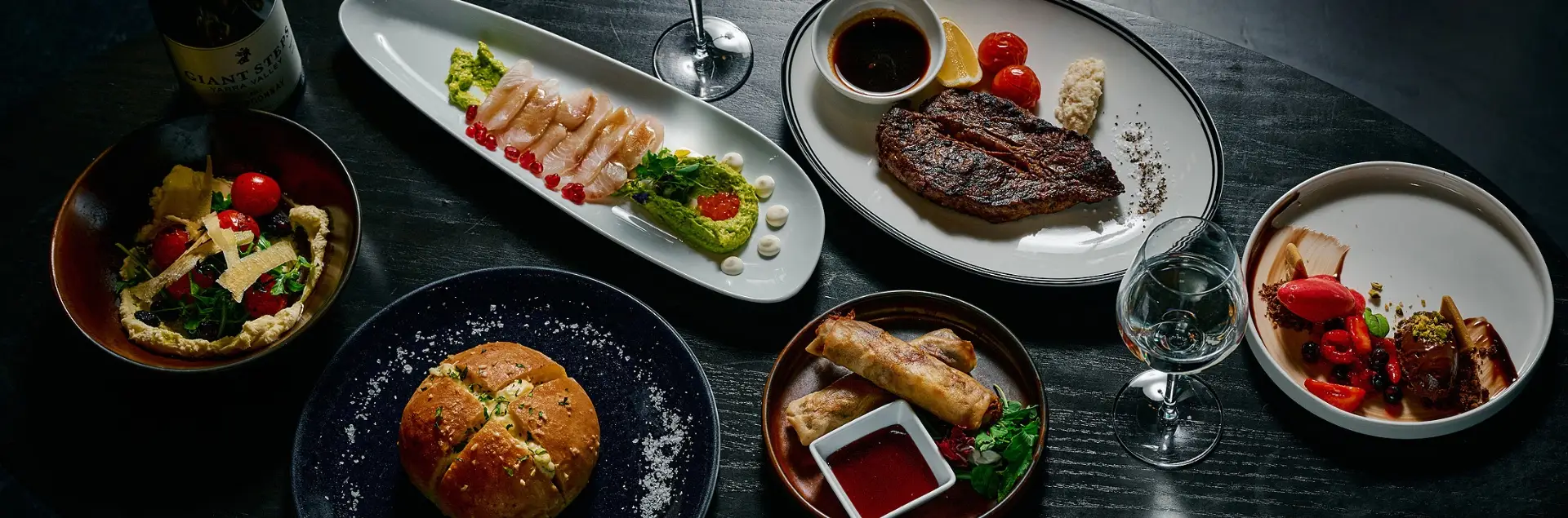 Table spread with steak, seafood, salad, bread, spring rolls and dessert