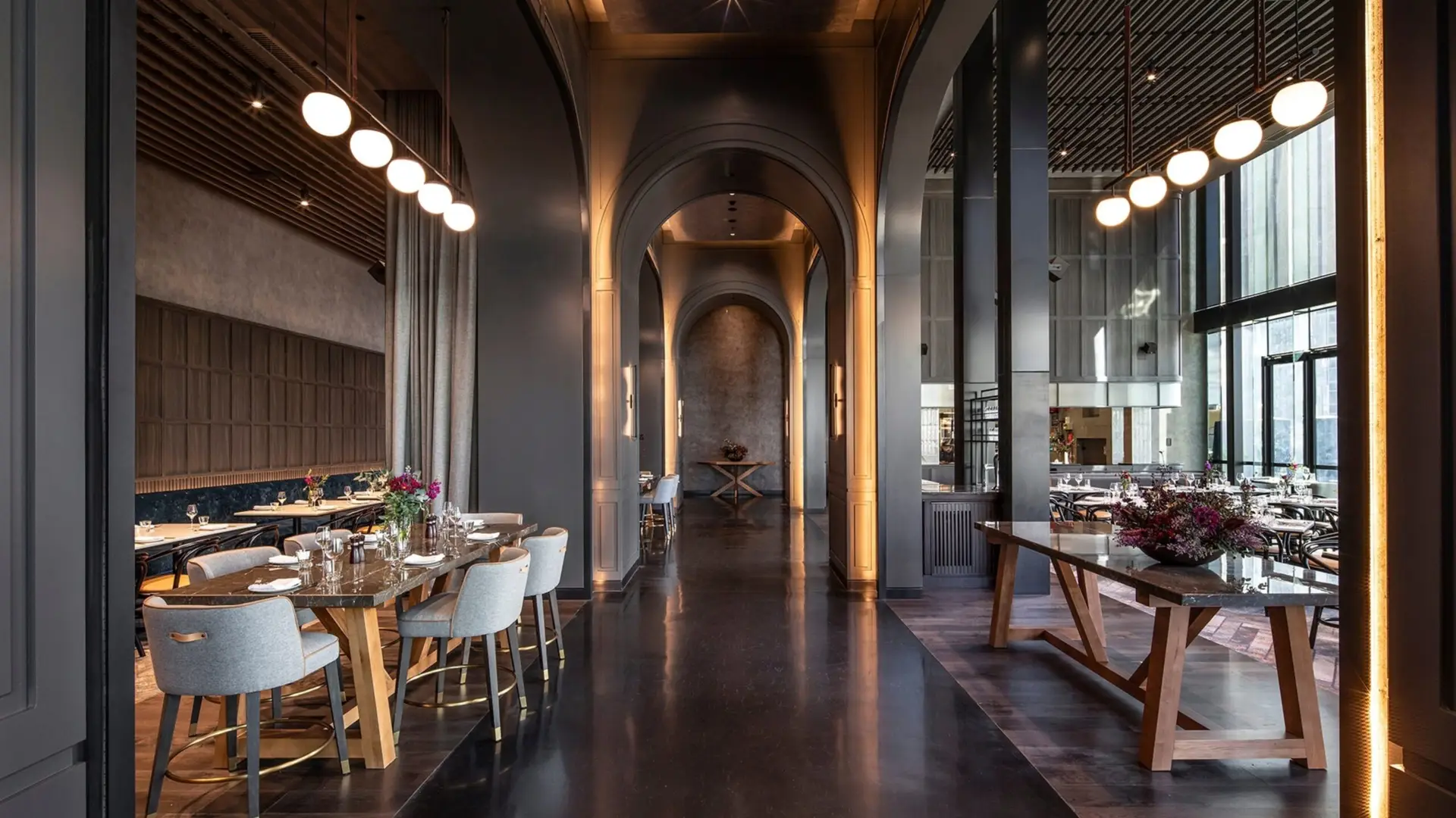 Restaurant interior with tall archways, dining tables, pendant lights and floor-to-ceiling windows