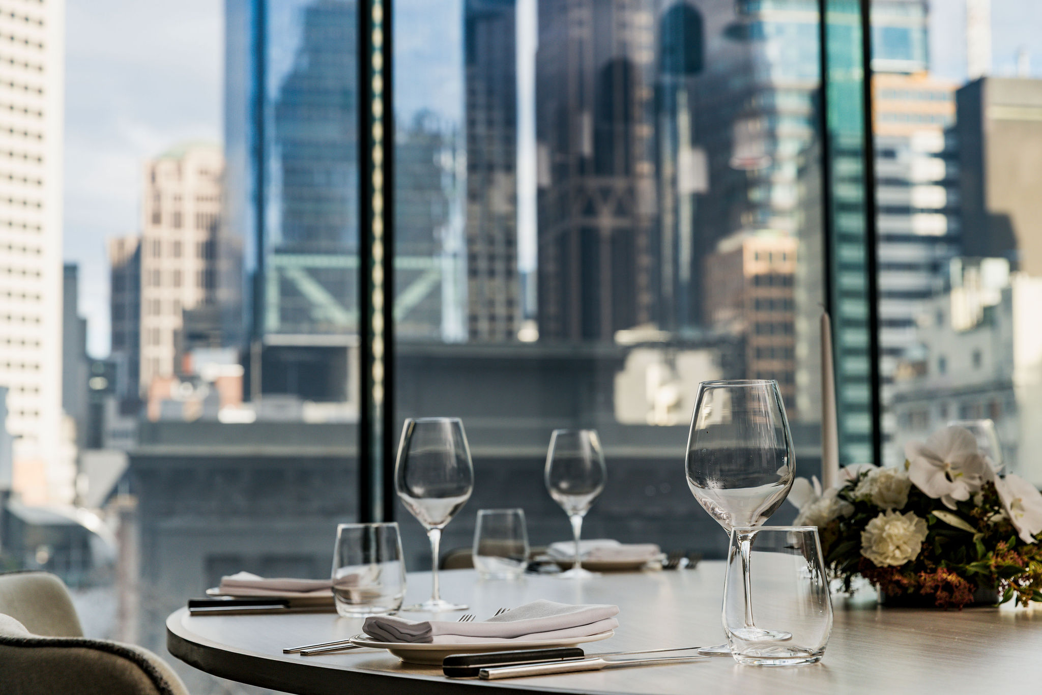 A private dining table set beside floor-to-ceiling windows over the Melbourne skyline