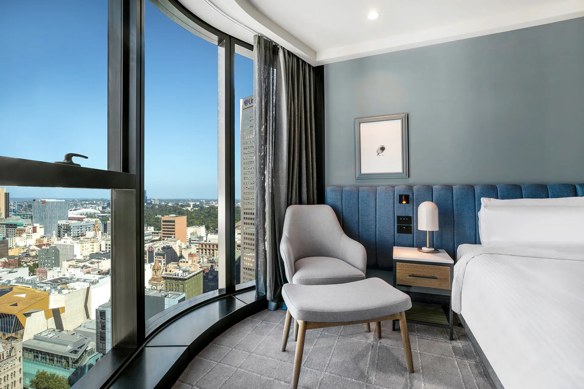 Guest room corner with curved floor-to-ceiling window, lounge chair and city view
