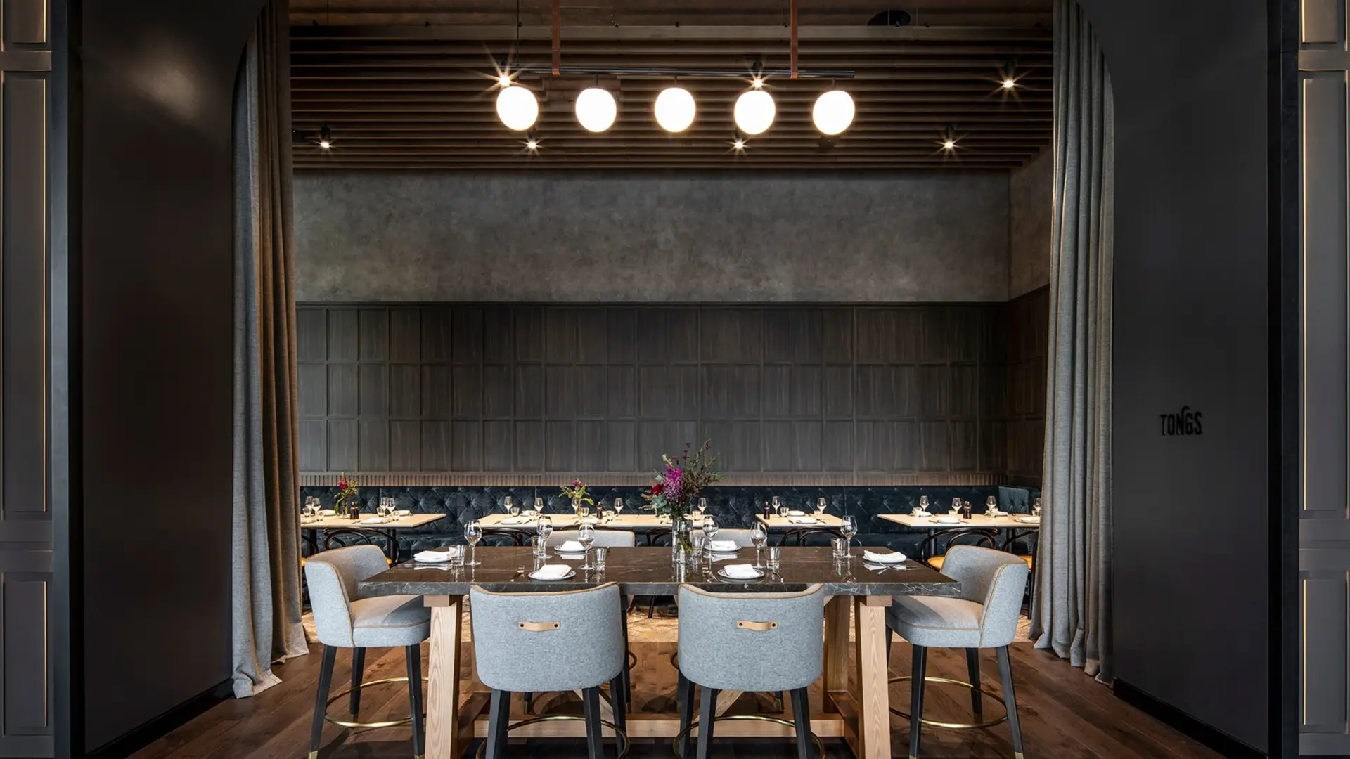 Private dining room with long tables, grey chairs, floral arrangements and pendant lighting