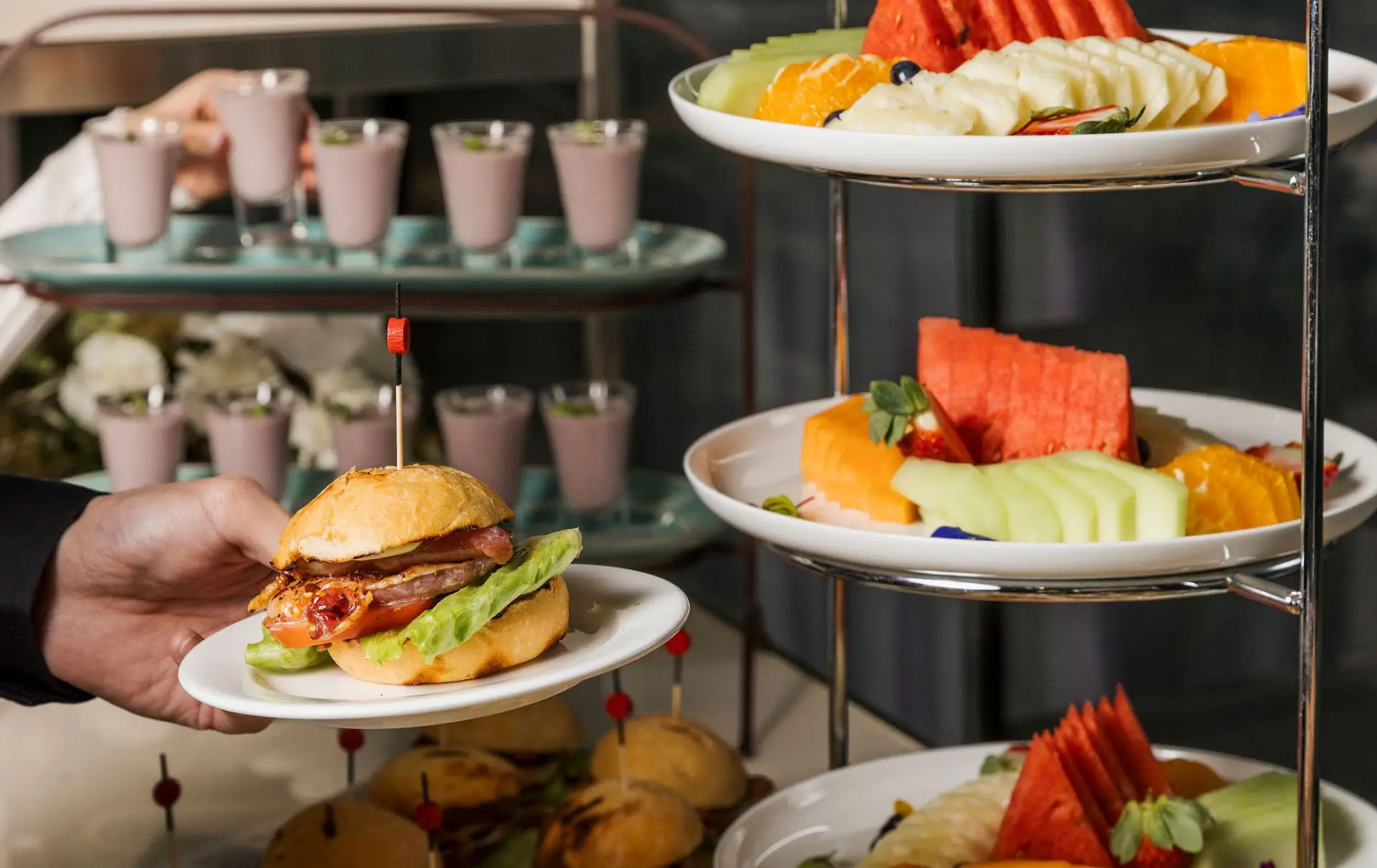 A tiered stand of sliders, fruit and dessert shots served at an event