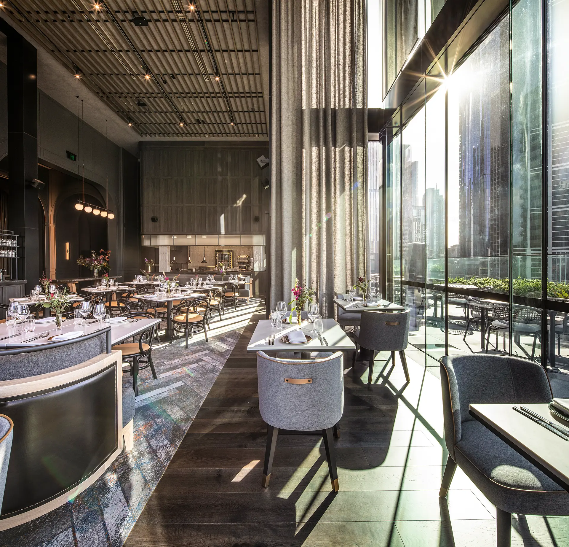 Sunlit restaurant dining area with floor-to-ceiling windows, city views and set tables