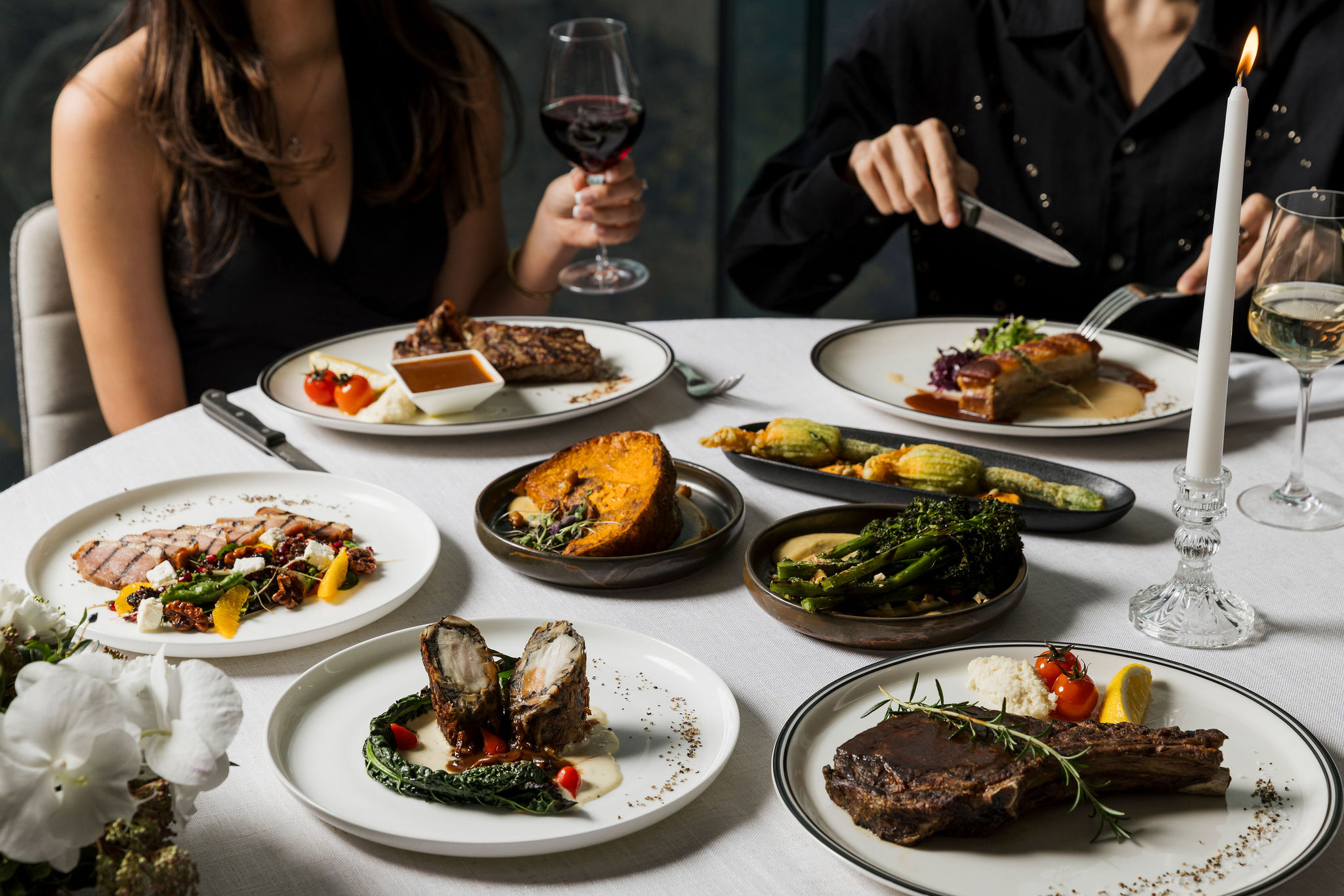 Guests sharing plates of steak, seafood and vegetables over wine