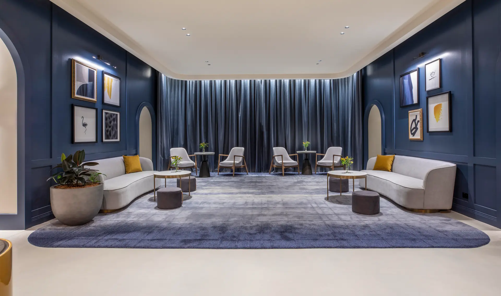 Spacious lounge with curved sofas, blue walls, framed artwork and floor-to-ceiling curtains