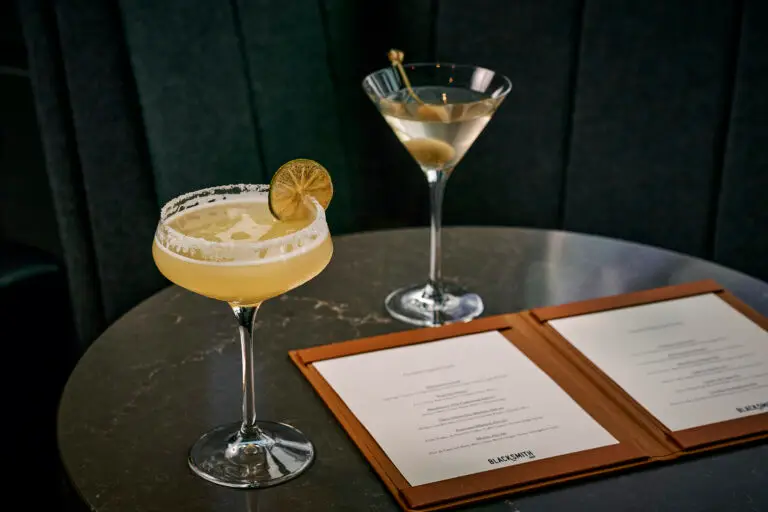 Two cocktails served on a table beside an open Blacksmith drinks menu
