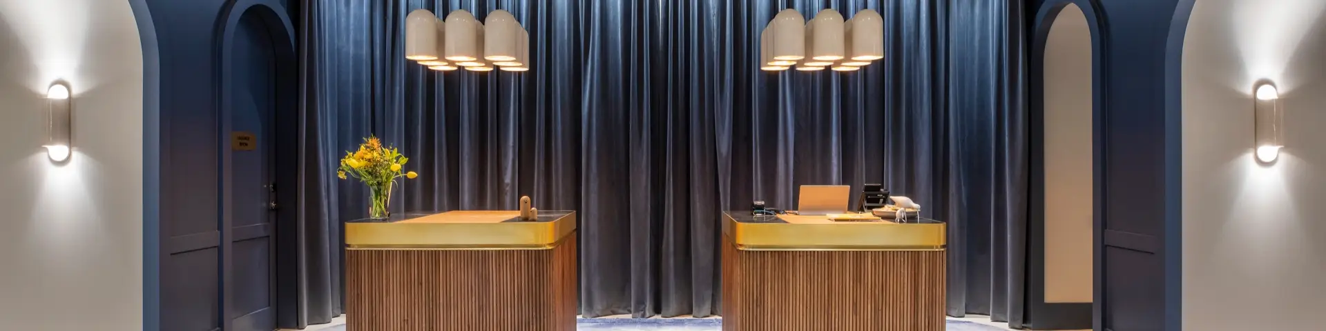 Two timber reception desks with brass tops framed by dark blue curtains and arched doorways