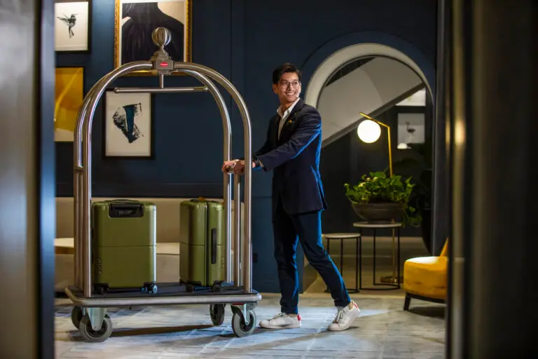 Hotel staff member pushing a luggage trolley with two green suitcases through the lobby