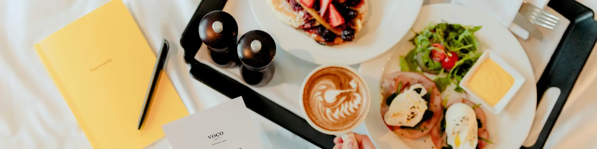 Breakfast tray with coffee, eggs, salad and pancakes beside voco Melbourne Central stationery