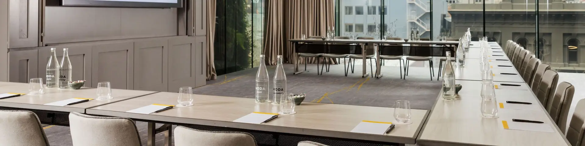 Meeting room arranged in a U-shape with chairs, notepads, pens, water bottles and glassware
