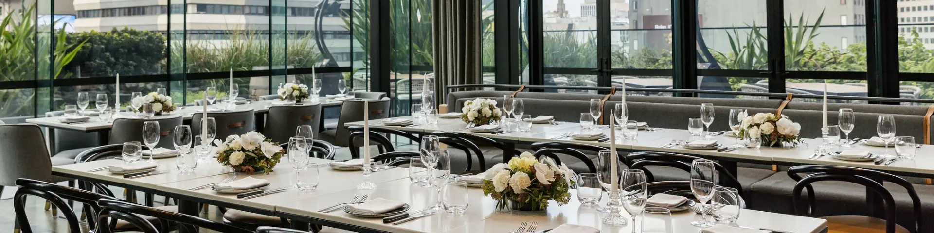 Private dining room with round tables, floral centrepieces, glassware and floor-to-ceiling windows