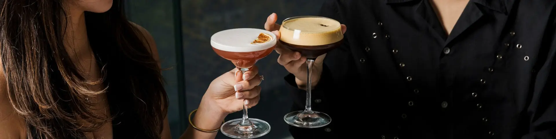 Two guests holding coupe glasses with contrasting cocktails during a social occasion