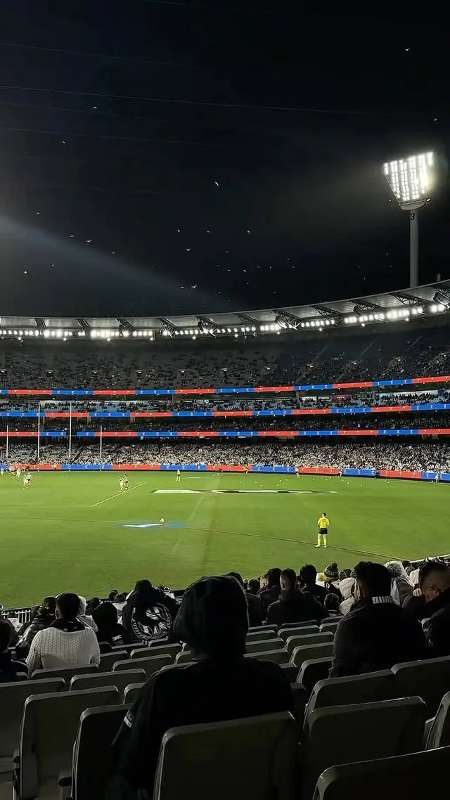 Spectators watching a sporting match on a floodlit stadium field at night