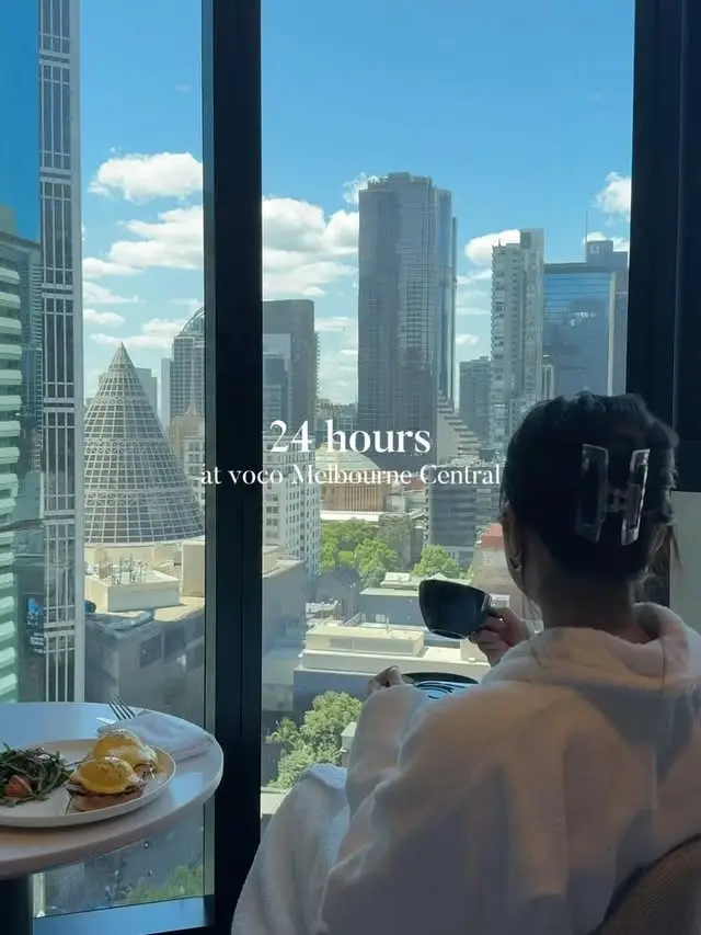 Guest enjoying breakfast by a floor-to-ceiling window overlooking Melbourne city buildings