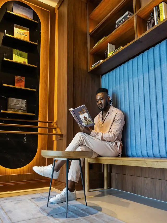 Guest reading a book on a blue upholstered bench beside timber bookshelves